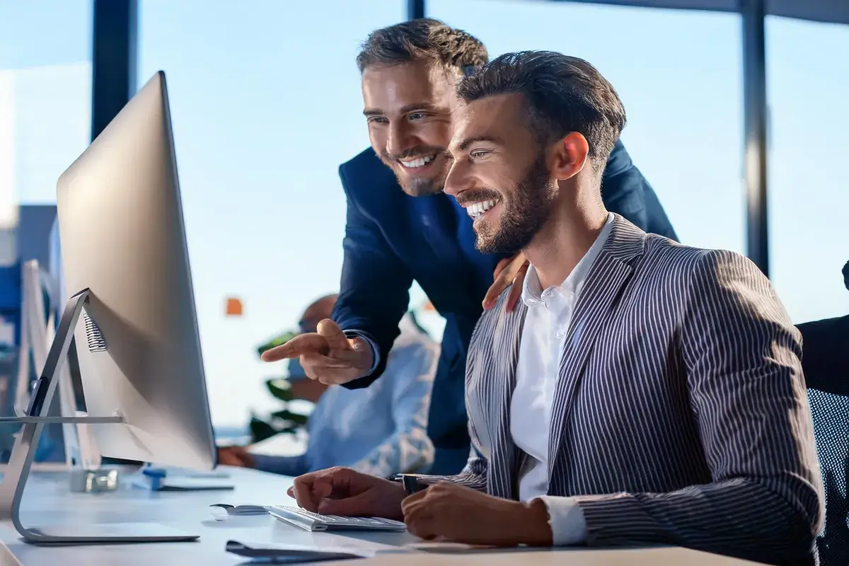 happy IT workers in office clothes looking at computer monitor